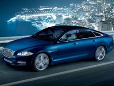 a blue car driving down the road at night with city lights in the back ground