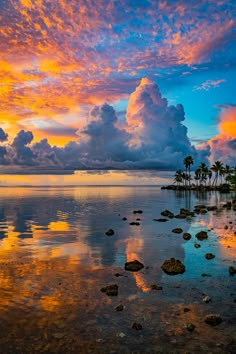 the sun is setting on an island with palm trees and clouds in the sky above it