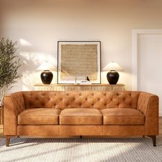 a tan leather couch sitting in a living room next to a table with two lamps on it