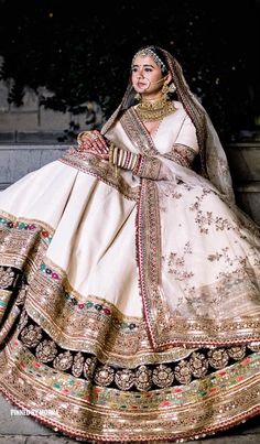 a woman in a white and gold wedding dress sitting on the ground with her hand on her hip