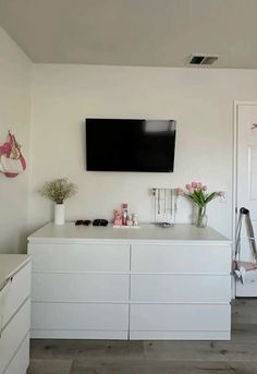 a flat screen tv mounted on the wall above a white dresser with drawers and drawers