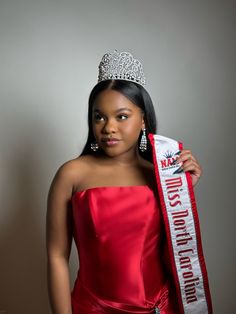 a woman in a red dress is holding up a miss america sash and wearing a tiara