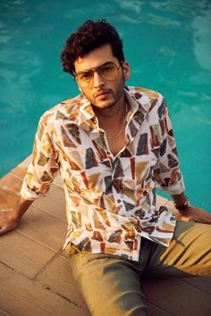 a man sitting on the edge of a swimming pool wearing glasses and a shirt with different colors