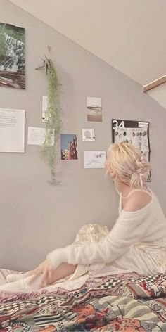 a woman sitting on top of a bed next to a wall covered in pictures and papers