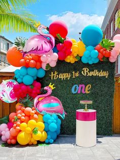 an outdoor birthday party with balloons and streamers on the wall, including flamingos