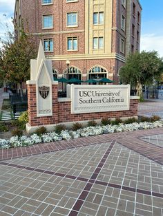 the sign for the university of southern california in front of a brick building with white flowers