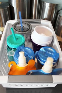 an organized dishwasher with cups, lids and utensils in front of stainless steel containers