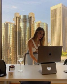 a woman sitting at a desk with a laptop computer in front of her, looking out the window