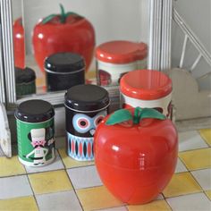 an apple, tomato and canisters sitting on a tiled floor in front of a mirror