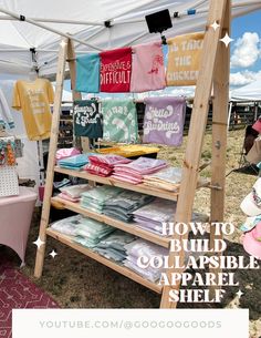 an outdoor tent with clothes and t - shirts for sale on the shelves below it