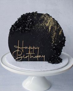 a black and gold happy birthday cake on a white pedestal with the words happy birthday written on it