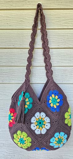 a crocheted purse hanging on the side of a building with flowers and tassels