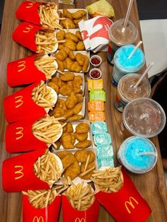 a table topped with trays of food next to plastic cups and drinks on top of a wooden table