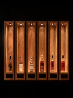 four bottles of alcohol lined up in wooden cases with lights on the wall behind them