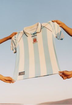 two hands holding up a blue and white striped shirt that is being held by another person