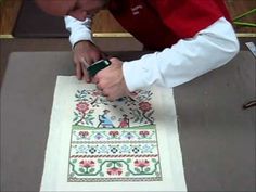 a woman is using a machine to make a cross stitch pattern on a piece of cloth