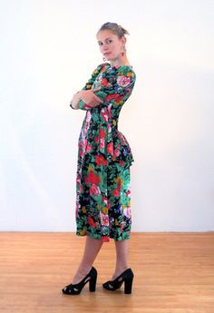 This is a delightful floral romantic vintage rayon "Starina" dress from the 1980s with 1940s style. A rainbow of lush garden flowers in shades of peach, green and purple drift across a black background. The soft rayon is matte textured and comfy. Princess seams and a basque waist shape the bodice front and back, and shoulder pads and gathered sleeve-caps put this sweet frock solidly in the 80s. Yet a flirty, flattering peplum skirt is pleated and attached at the waist, draping beautifully in the Green Floral Print Vintage Dress For Garden Party, Retro Floral Midi Dress For Party, Vintage Long Sleeve Floral Dress For Garden Party, Retro Green Midi Dress With Floral Print, Vintage Long Sleeve Floral Dress, Romantic Garden Party, Peplum Midi Dress, Basque Waist, 40s Style