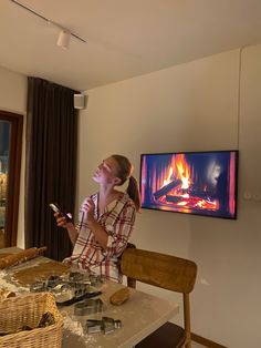 a woman sitting at a table in front of a tv holding a cell phone to her ear