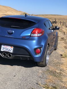 the back end of a blue sports car parked in front of a fenced off field