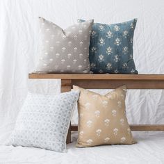 four pillows on a wooden bench against a white backdrop, one in blue and the other in beige