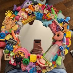 a person holding a cell phone in front of a mirror covered in toys and letters