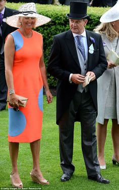 two women and a man are standing in the grass with hats on their heads, one is wearing an orange dress