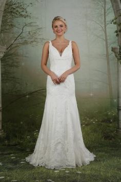 a woman in a white wedding dress posing for the camera with trees and grass behind her