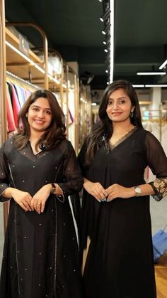 two women standing next to each other in front of clothing racks