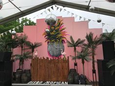 a large pineapple hanging from the side of a pink building with disco balls and palm trees