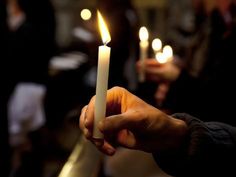 a person holding a lit candle in their hand with other people standing around behind them