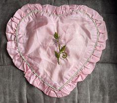 a pink heart shaped pillow with a flower on the front and green stems in the middle