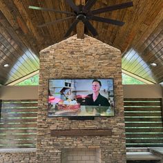 a large television mounted to the side of a brick fireplace in a room with wooden ceilings