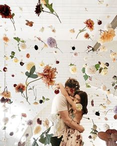 a man and woman standing in front of a wall with flowers hanging from the ceiling