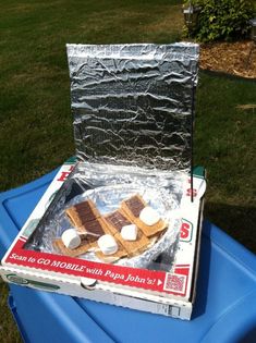 an open box with marshmallows and chocolate on it sitting on top of a blue trash can