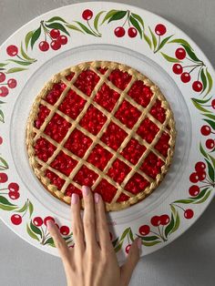 a person touching the top of a pie on a plate with cherries around it