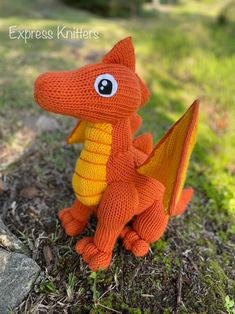 an orange knitted dragon sitting in the grass