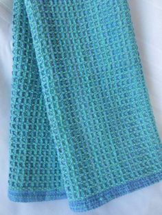 a blue and green knitted blanket laying on top of a white bed coverlet