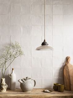 a wooden table topped with white vases next to a wall mounted light hanging from a chain