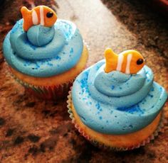 two cupcakes with blue frosting and orange fish on them sitting on a counter