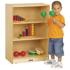 a young boy holding two green plastic marabels in front of a bookcase