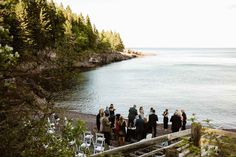 a group of people standing on top of a beach next to the ocean and trees