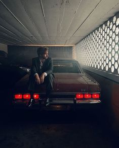 a man sitting on the back of a car in a parking garage next to a wall