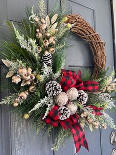 a wreath with pine cones and evergreens on the front door is adorned with red and black plaid ribbon