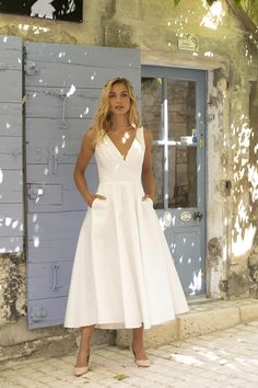 a woman standing in front of a blue door wearing a white dress