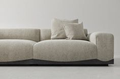 a couch with two pillows on top of it in front of a white wall and floor