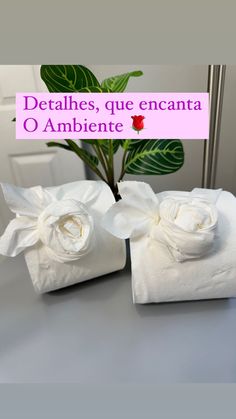 two napkins with white flowers on them sitting on a table next to a potted plant