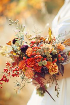 a bridal holding a bouquet of flowers and berries in the fall colors with leaves on it