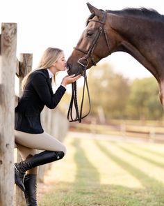 a woman is sitting on a fence and petting a horse's bridle