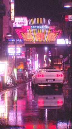 a car is driving down the street in front of a neon sign and gas pumps