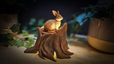 a rabbit sitting on top of a piece of wood next to a potted plant